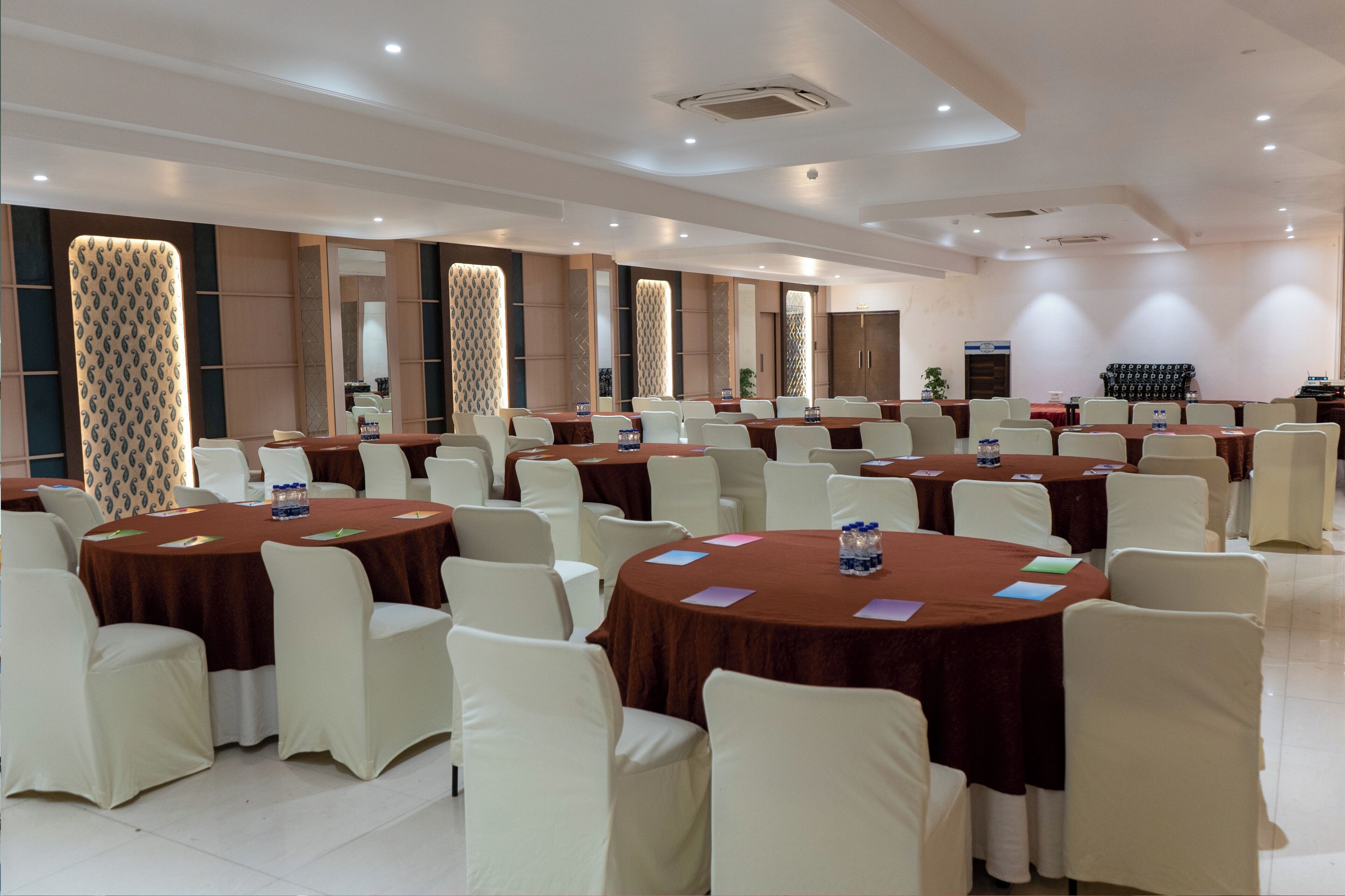 A conference room with multiple round tables, white chairs, and brown tablecloths.