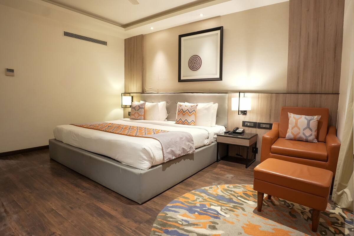 Habitación de hotel con una cama grande, una silla, una mesita de noche y un cuadro colgado en la pared.