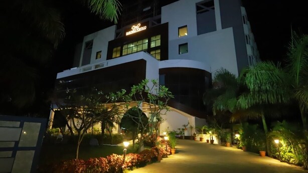 A modern hotel with a prominent sign, a well-lit entrance, and a landscaped garden with potted plants and a pathway. - Grand Sarovar Portico (Latur)