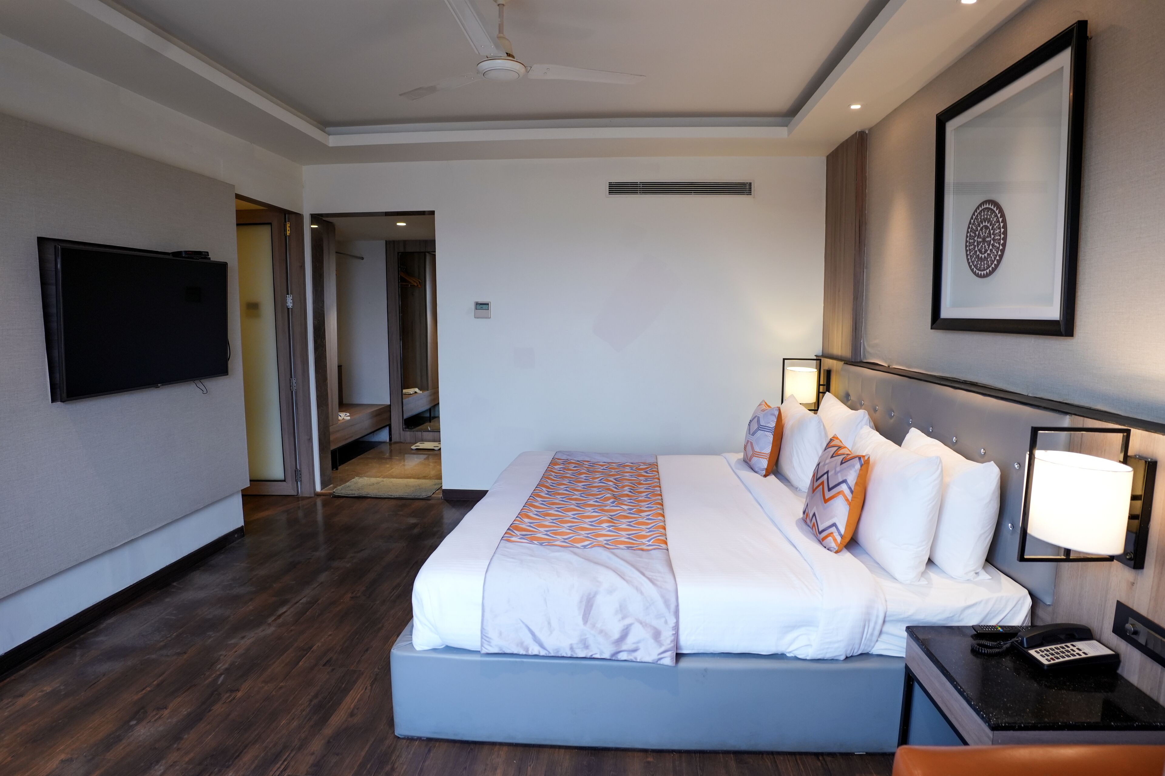 Habitación de hotel con cama, televisor, escritorio con lámpara y un cuadro en la pared.