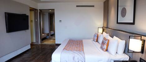 Habitación de hotel con cama, televisor, escritorio con lámpara y un cuadro en la pared.
