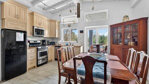 A kitchen with wooden cabinets, a black refrigerator, a microwave, and an oven. There is a dining table with chairs and a view of the outdoors through a window. - Miles of Private Gulf Beach-Luxury 4 BR-Pets Okay-Kayaks & SUPs-Best Shark Teeth (Englewood)