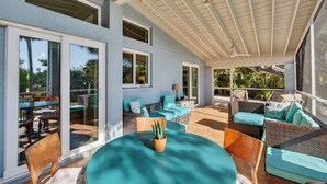 A covered patio with outdoor furniture, a table with a potted plant, and large windows. - Miles of Private Gulf Beach-Luxury 4 BR-Pets Okay-Kayaks & SUPs-Best Shark Teeth (Englewood)