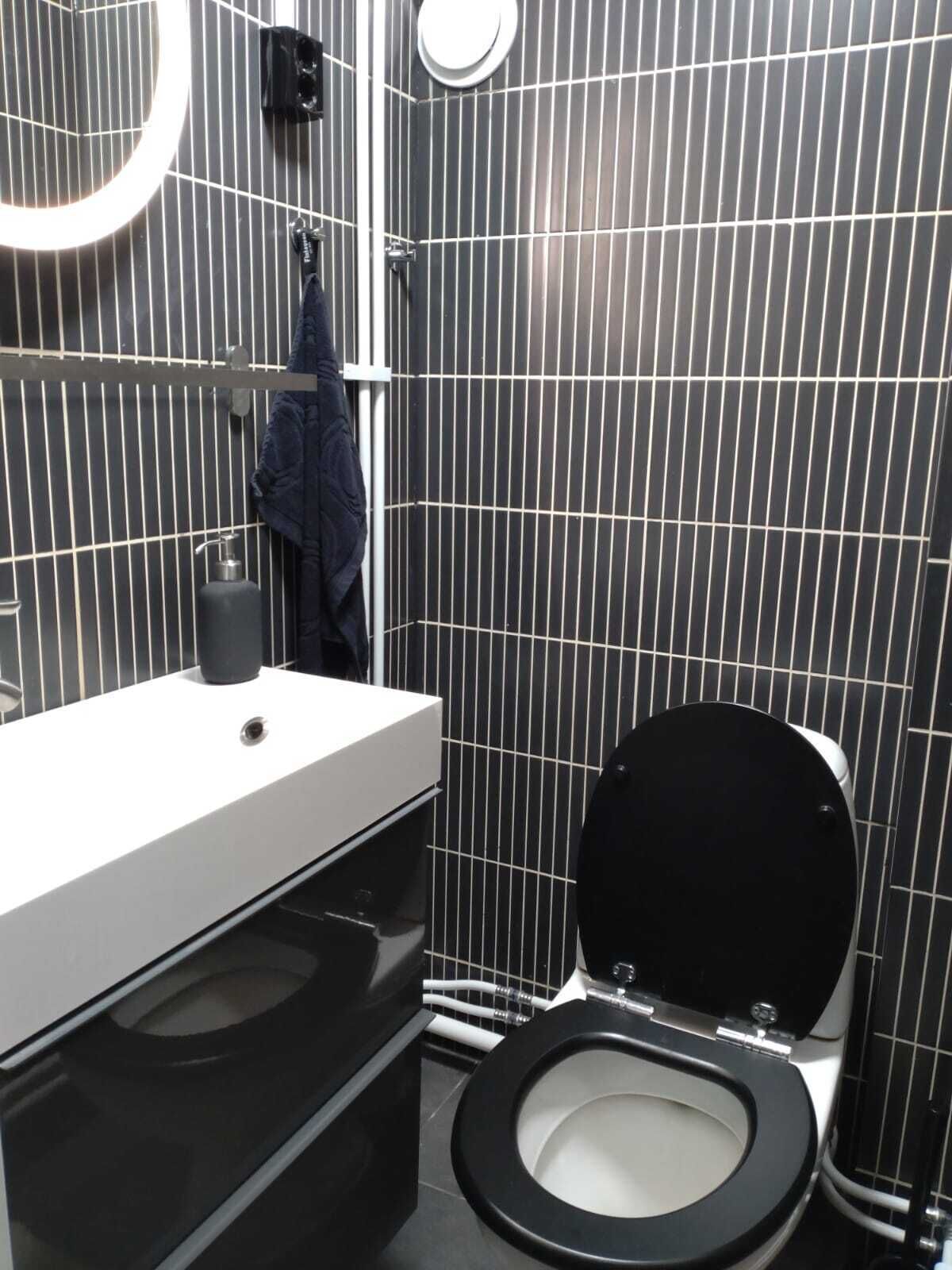 Ein modernes Badezimmer mit einer schwarzen Toilette, einem weißen Waschbecken und einem Handtuch an der Wand.