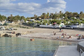 Een strand met mensen die ontspannen, een boot en campers langs de kust.