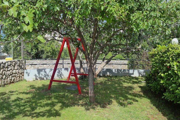 A tree with a red swing set in a grassy area.