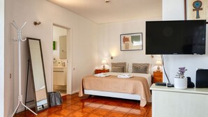 A hotel room with a bed, a television, a desk with a phone, and a mirror.