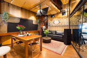 A dining area with a wooden table, chairs, and a small round table with a plant. There is a black leather couch and a large speaker in the background. - VILA MADALENA: PERFECT LOCATION, STYLISH APARTMENT (São Paulo)