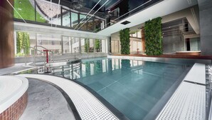 Une piscine intérieure moderne avec des parois en verre transparent, un escalier central et un mur végétal.