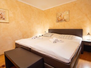 A neatly made bed with pillows and towels, a bedside table with a lamp, and a painting on the wall. - Residenz Laguna Whg L-19 .. - L-19 (Kühlungsborn)