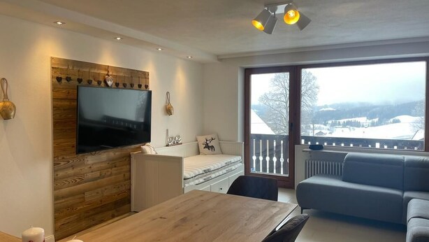 Un salon moderne avec un meuble mural en bois, un téléviseur à écran plat, un canapé, une table à manger décorée de bougies et un balcon avec vue.