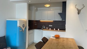 Une cuisine moderne avec des meubles blancs, un réfrigérateur bleu et une table à manger en bois, accompagnée de chaises.