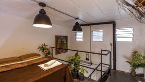 Ein Zimmer mit einem hölzernen Bett, zwei Pendelleuchten, einem Gemälde und einer Treppe mit Metallgeländer.