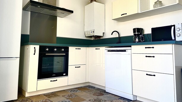 A compact kitchen with white cabinets, a black stove, a dishwasher, and a microwave. - 77m2 T4 apartment (La Seyne-sur-Mer)