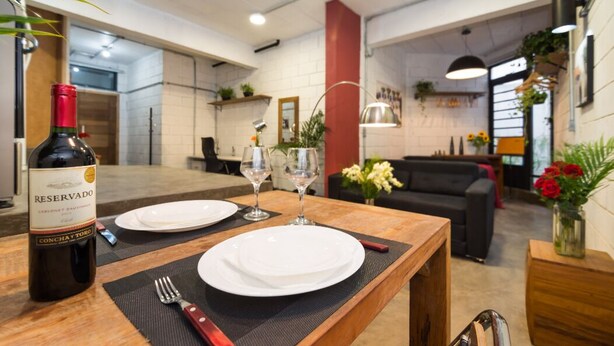 A dining area with a wooden table, two white plates, a bottle of wine, and two wine glasses. - VILA MADALENA Perfect Location: Artistic Apartment (SP)