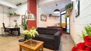 A modern living room with a black sofa, a wooden coffee table, and a desk with a chair. There are plants, a hanging light, and a painting on the wall. - VILA MADALENA Perfect Location: Artistic Apartment (SP)