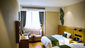 Une chambre d’hôtel avec deux lits, un bureau, une chaise, une petite table avec un vase et une grande fenêtre avec des rideaux.