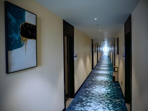 A long, narrow hallway with a blue and white patterned carpet, framed artwork on the left wall, and doors on both sides. - Greentree Inn Fuyang Yingdong District Xingfu Road Century Fortune Plaza (Fuyang)