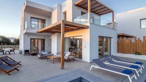 Una casa moderna de dos pisos con piscina, mobiliario exterior y terraza de madera.