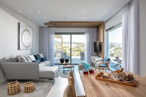 A modern living room with a grey sofa, wooden coffee table, and a dining area with a wooden table set for a meal.