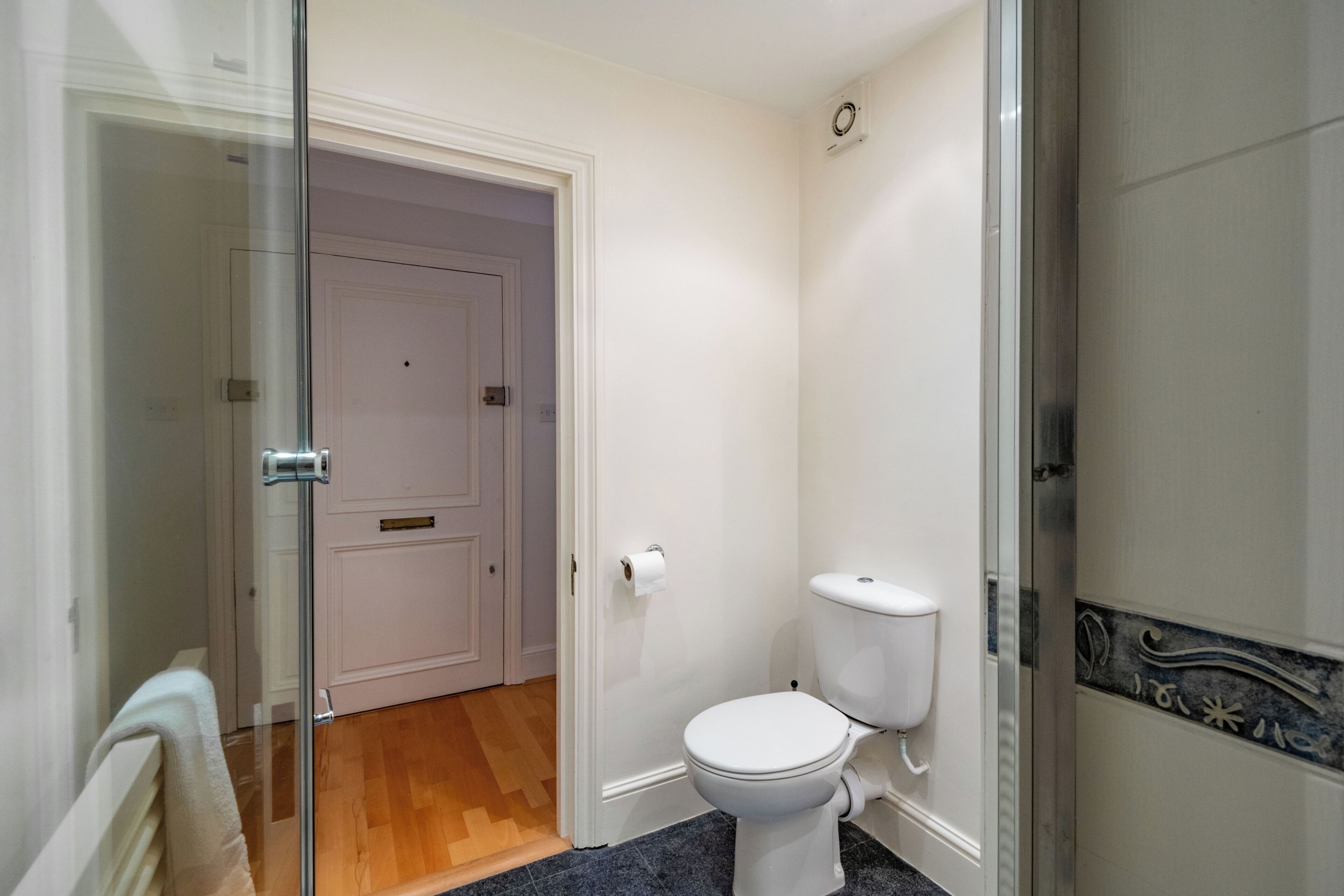 A bathroom with a white toilet, a glass shower enclosure, and a wooden floor.