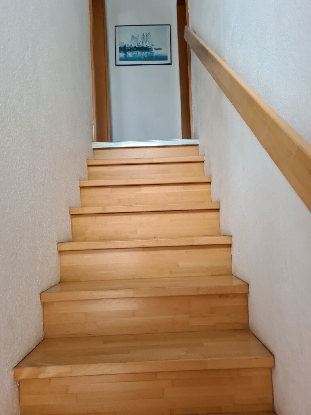 Un escalier en bois, doté d’une rampe, mène à un palier où est accrochée une image encadrée.