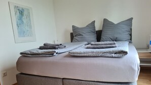 Un lit avec une literie et des oreillers gris, une couverture grise pliée et un banc recouvert d’un tissu gris.