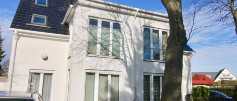 A two-story house with large windows and a tree in front.