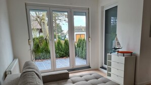 Ein modernes Wohnzimmer mit einer grauen Eckcouch, einem weißen Couchtisch und einer Schiebeglastür, die zu einem Garten führt.