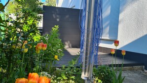 Ein Garten mit Tulpen und verschiedenen Pflanzen, einer Metallkonstruktion sowie ein Gebäude mit dunkler Fassade und blauen Fensterläden.
