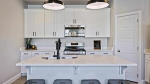 Une cuisine moderne avec des meubles blancs, un îlot central doté de tabourets, des appareils en acier inoxydable et un éclairage suspendu.
