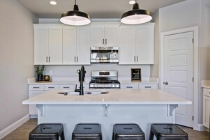 A modern kitchen with white cabinets, a central island with stools, stainless steel appliances, and pendant lighting.