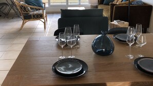 Ein Essbereich mit einem Holztisch, gedeckt für sechs Personen, einem Korbstuhl, einer Couch und einem großen Fenster mit Vorhängen.