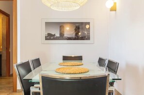 En matplats med ett runt bord, stolar, en inramad bild av en stadsbild och en hängande lampa.