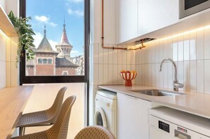 Une cuisine moderne Ă©quipĂ©e dâun lave-linge, dâun Ă©vier et dâune fenĂȘtre donnant sur un immeuble.