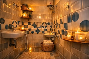 A bathroom with two sinks, a shower, a tiled wall with a geometric pattern, and a shelf with candles and toiletries.