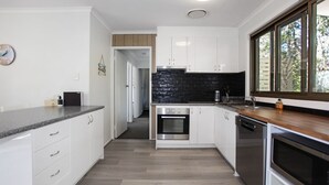 A modern kitchen with white cabinets, a black backsplash, and a wooden countertop. - Barralong Beach House (Hawks Nest)