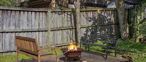 A backyard with a wooden bench, a metal fire pit, and a wooden fence.