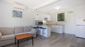 A compact living space with a kitchenette, a sofa, a coffee table, and a bar stool. - Barralong Beach House (Hawks Nest)
