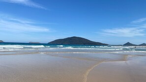 A beach with clear blue water, sandy shore, and distant hills. - Barralong Beach House (Hawks Nest)