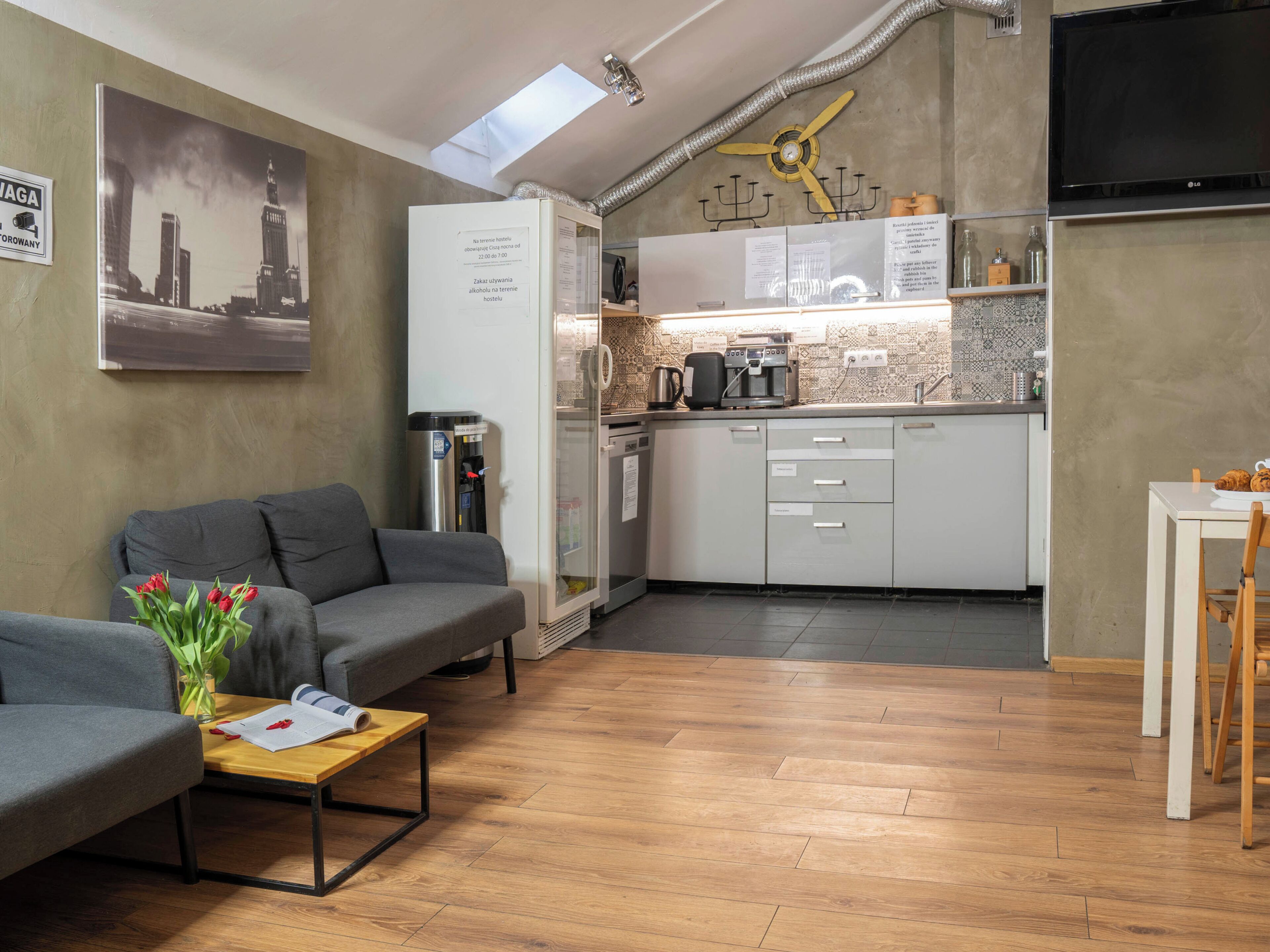 A compact living space with a kitchenette, a grey sofa, a small dining table, and a coffee machine.