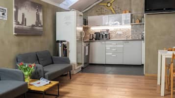 A compact living space with a kitchenette, a grey sofa, a small dining table, and a coffee machine.