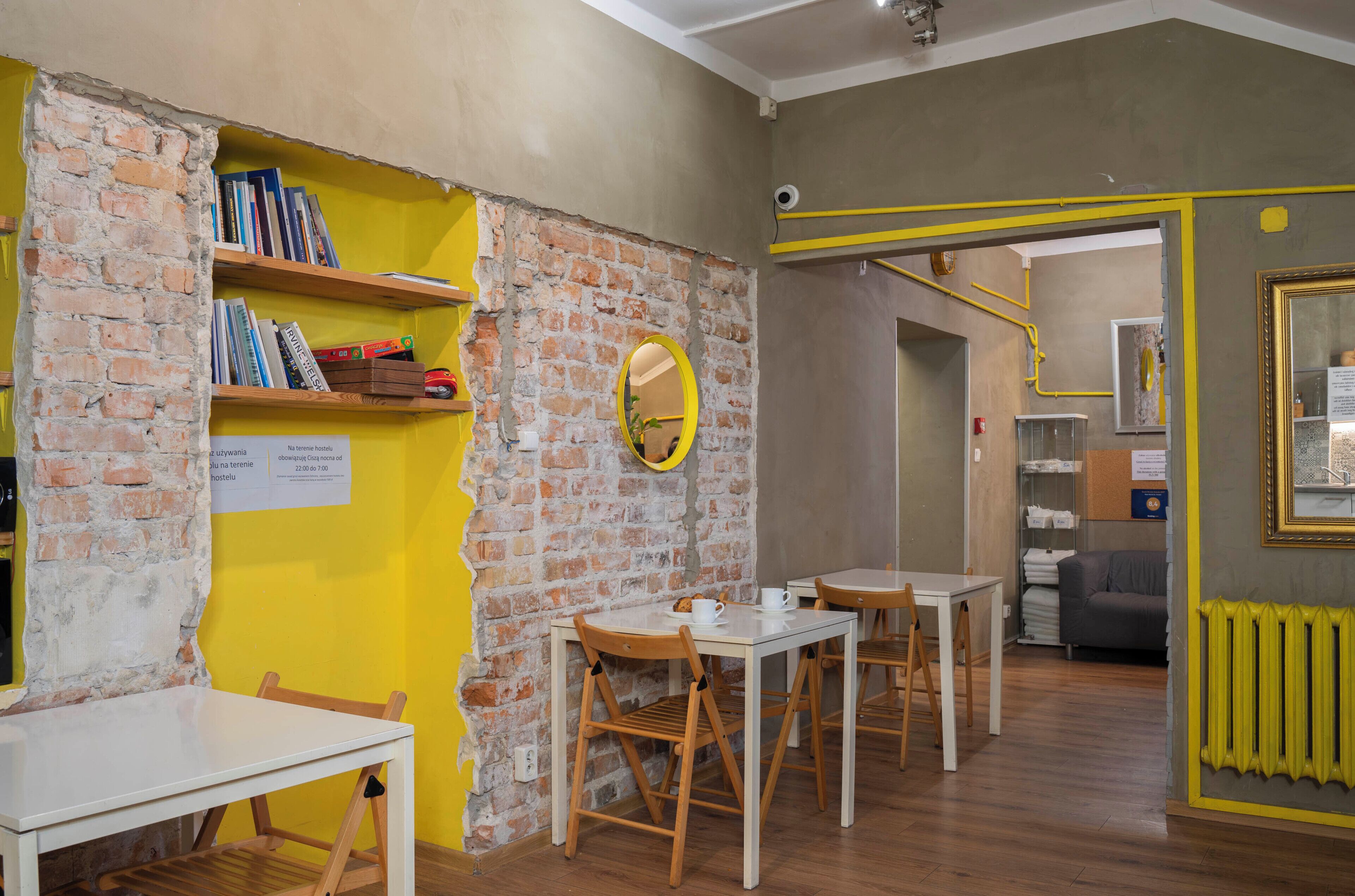 A room with a brick wall, wooden shelves with books, a round mirror, and a table with chairs.