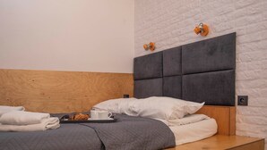 A neatly made bed with a grey quilt, white pillows, and a tray with a cup and a plate of food.