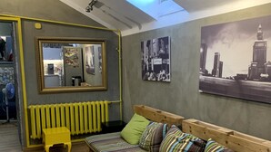 A cozy room with a wooden pallet sofa, a small yellow stool, and a wooden coffee table. There is a mirror on the wall and a framed picture above the sofa.