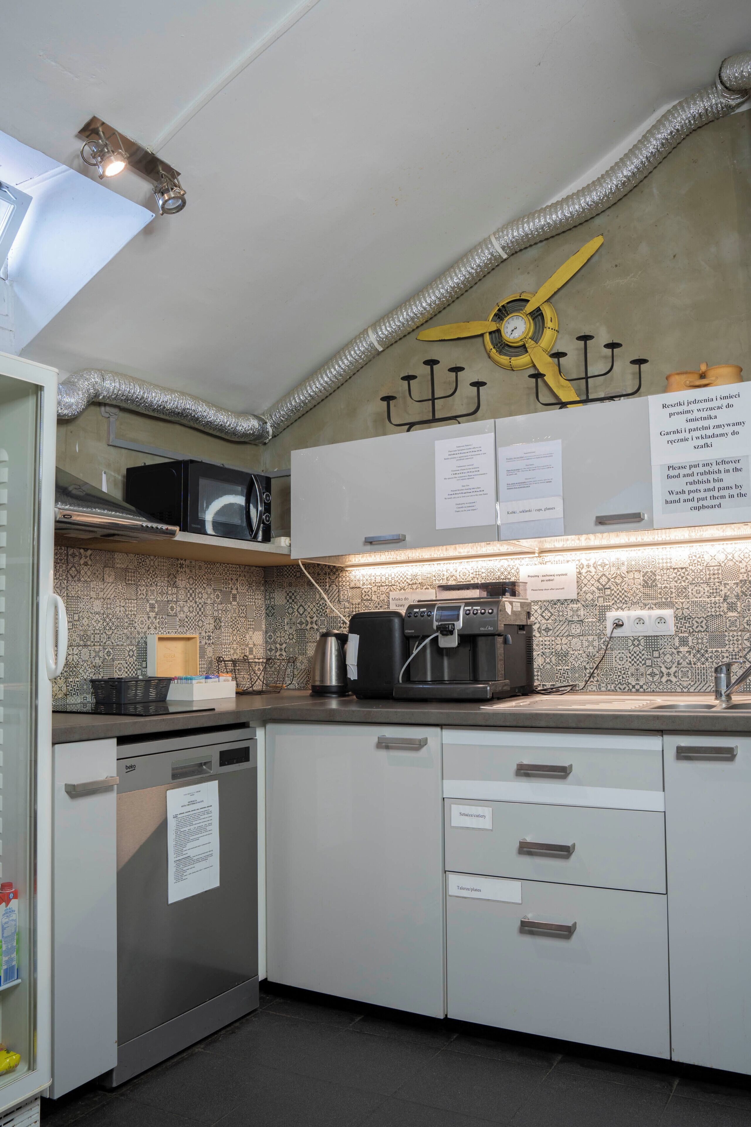 A kitchen with a microwave, coffee machine, and a note on the wall.
