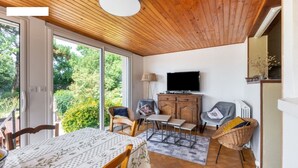 Ein gemütliches Wohnzimmer mit Holzbalkendecke, einem Fernseher und einem Essbereich mit Tisch und Stühlen.
