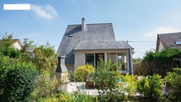 Ein zweigeschossiges Haus mit einem geneigten Dach, einem Schornstein und einem Balkon.