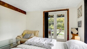 A bedroom with a bed, a glass table, a chair, and a view of the outdoors through a door.