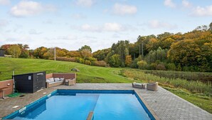 A rectangular swimming pool with a paved deck, surrounded by a grassy area and trees with autumn foliage.